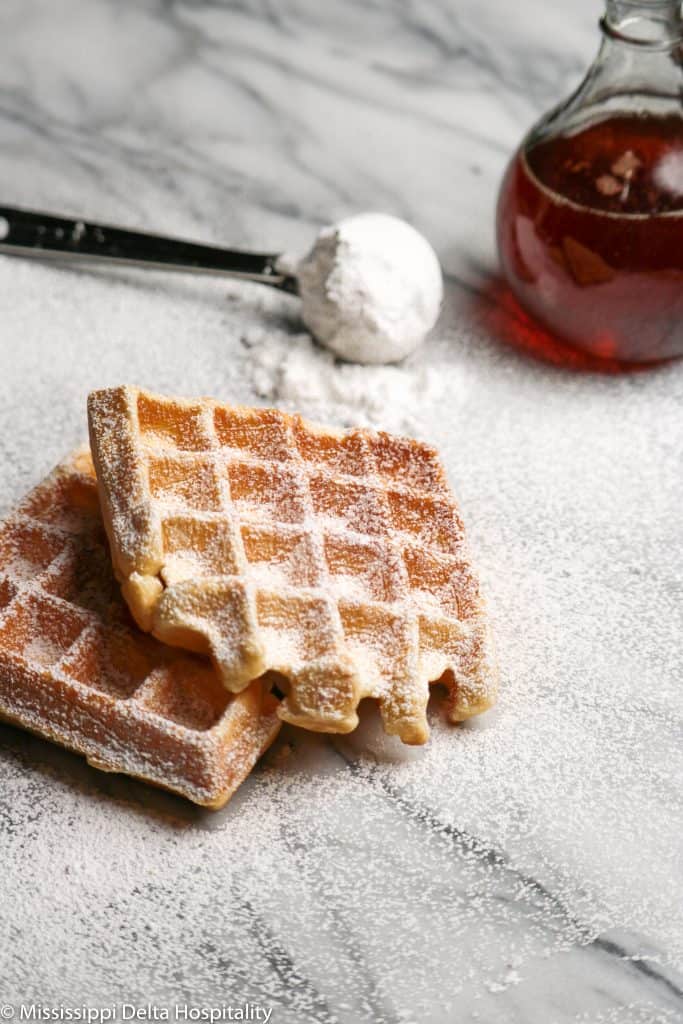 two belgian waffles on a marble board with powdered sugar