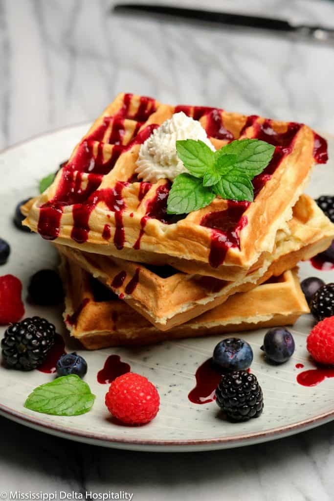 three Belgian waffles with mixed berries, berry puree, whipped cream, and a sprig of mint