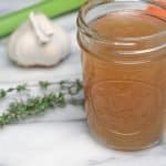 a jar of chicken stock with garlic, thyme, and celery