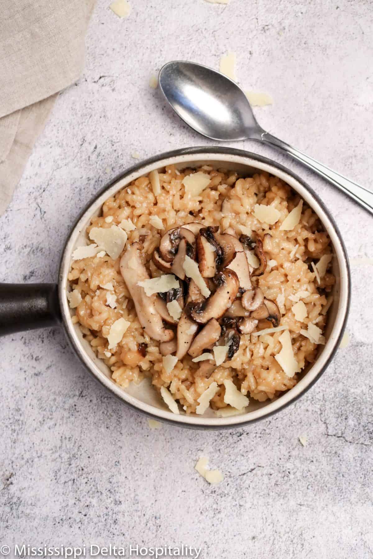 a bowl of mushroom risotto with parmesan shavings on top and a silver spoon.