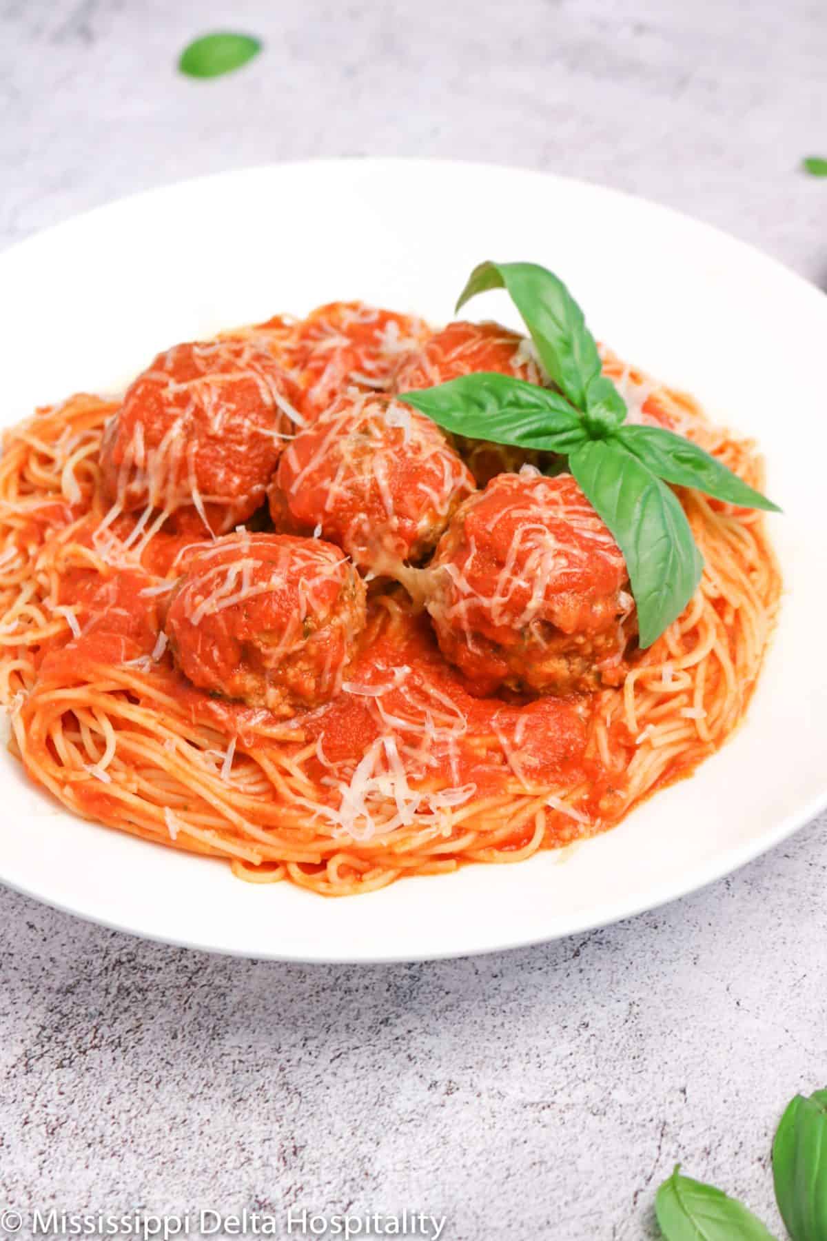 a bowl of spaghetti and meatballs with basil leaves and cheese on top on a concrete board.