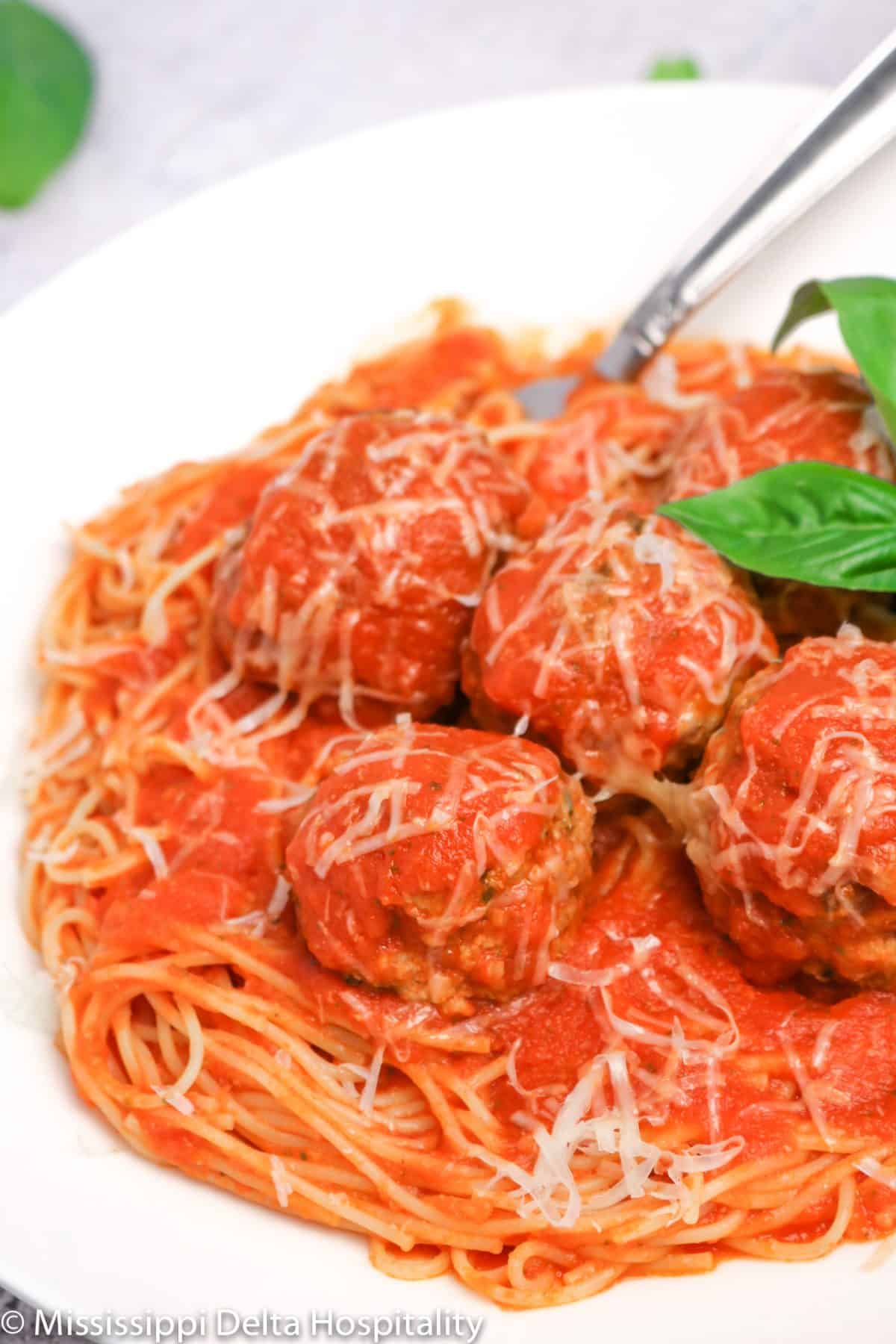 a bowl of spaghetti and meatballs with basil leaves and cheese on top with a fork in it on a concrete board.