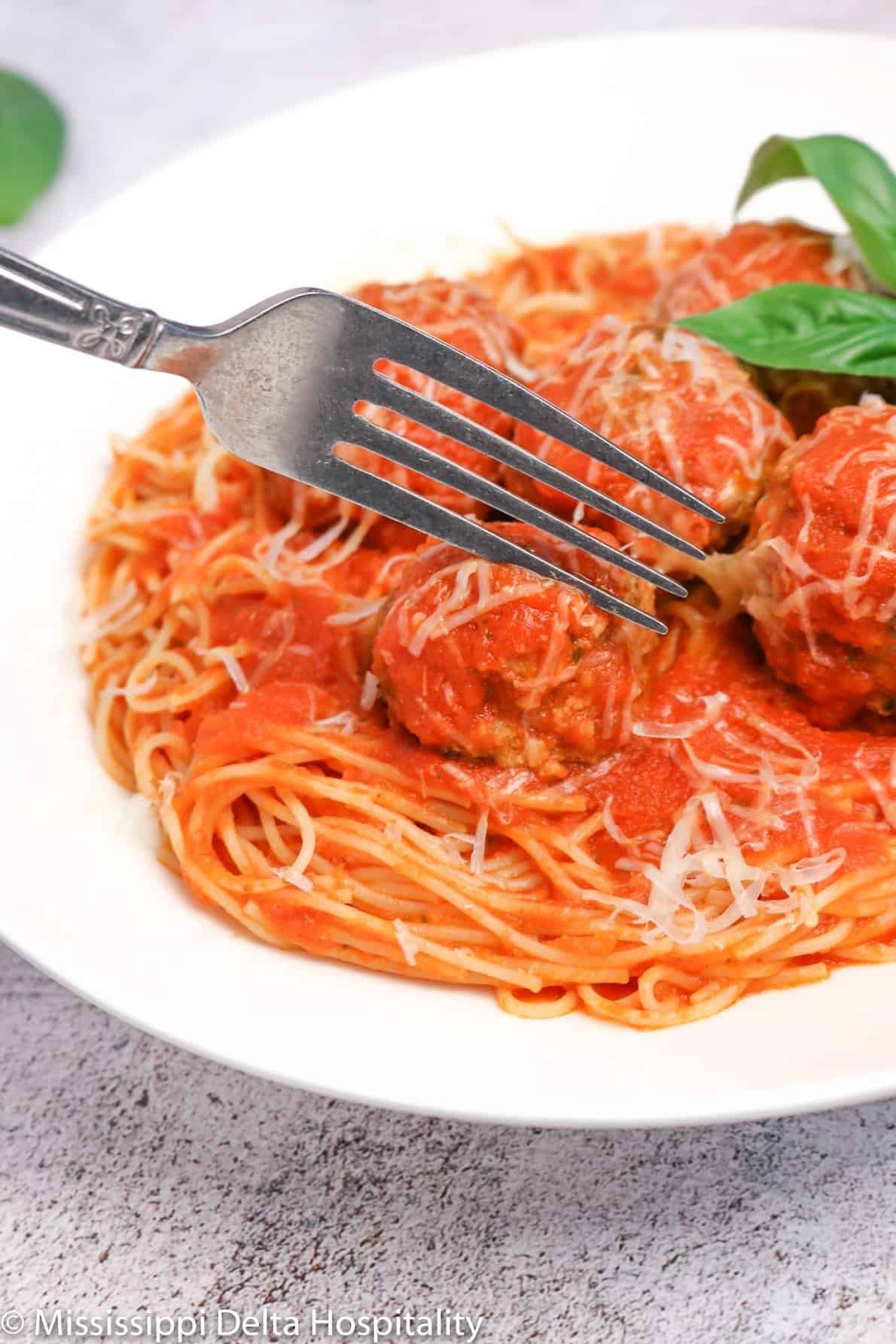 a bowl of spaghetti and meatballs with a fork in it on a concrete board.