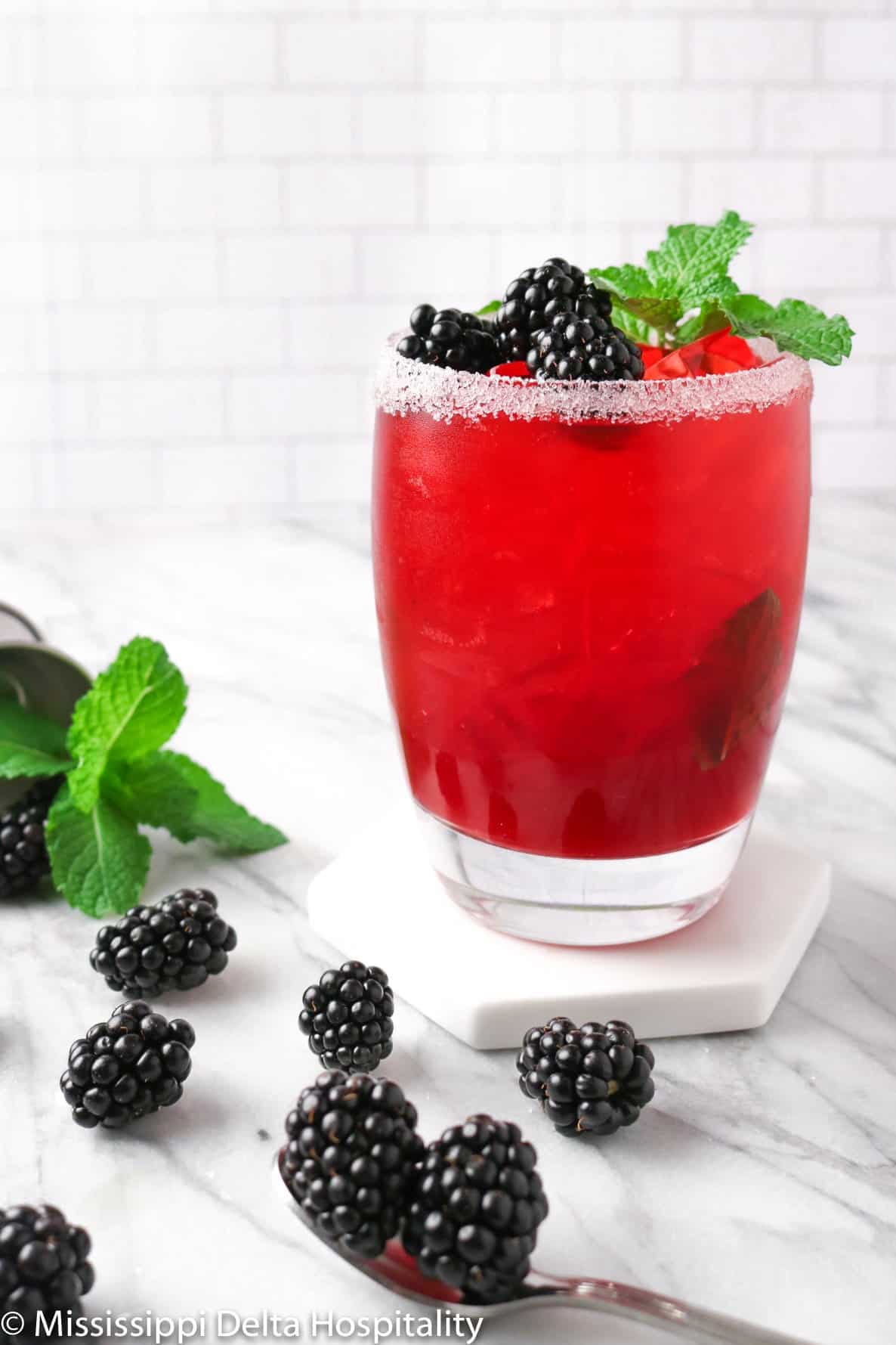 a glass of a blackberry bourbon cocktail with blackberries and mint on a marble board.