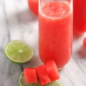 three glasses with slushie in them and slices of lime on a marble board.