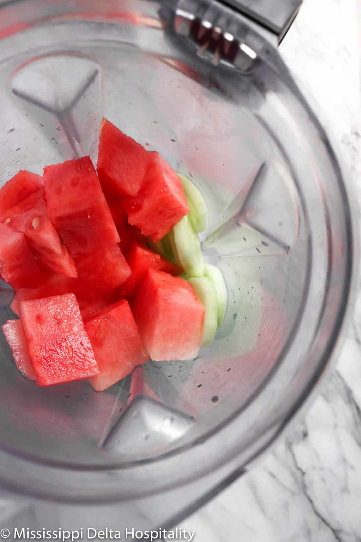 a blender with watermelon chunks and slices of cucumber in it