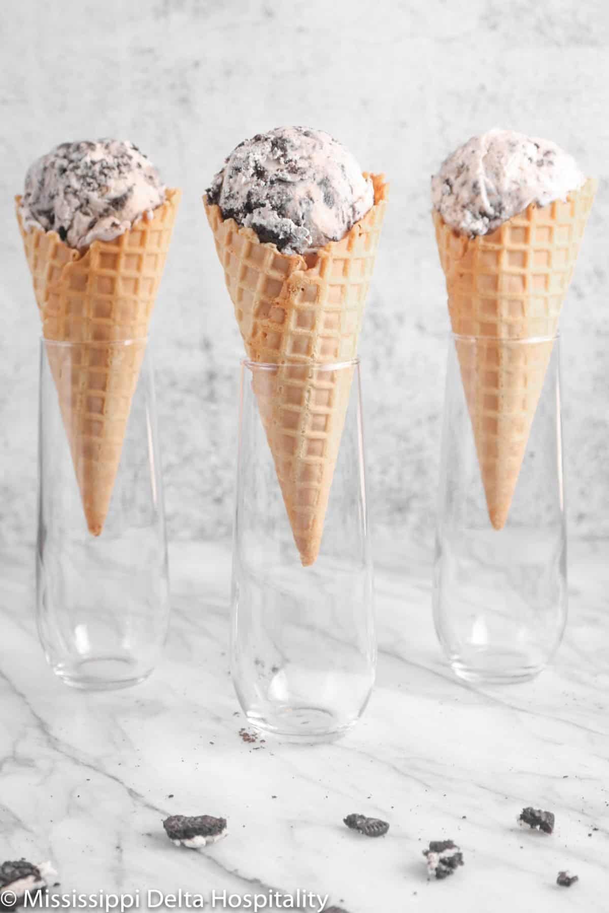 three waffle cones with three scoops of cookies in cream in three glasses on a marble board