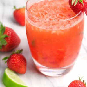 A glass of strawberry mint julep with strawberries and a lime slice