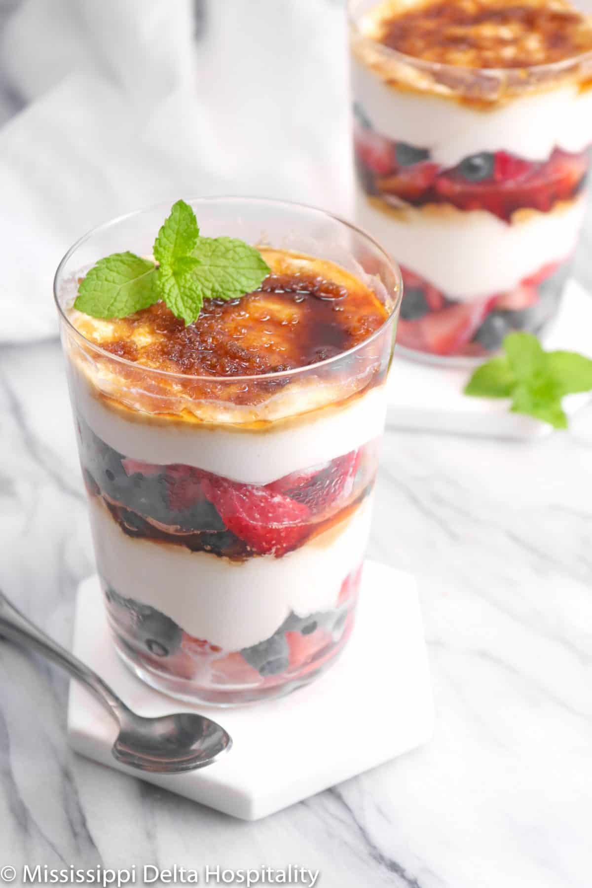two glasses of berry parfaits on a marble board with mint and a spoon