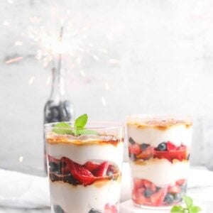 two glasses of berries and cream parfait with a jar of blueberries and a sparkler
