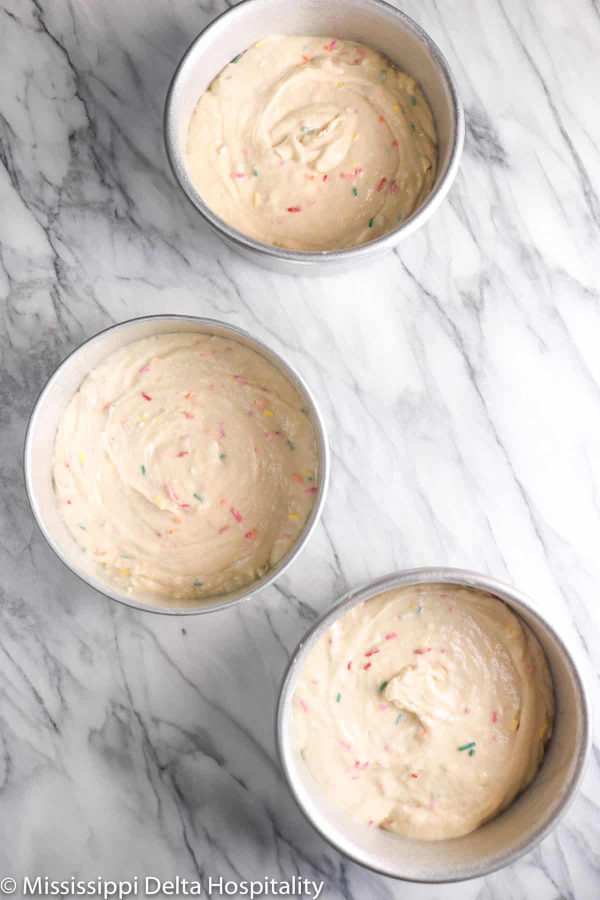 funfetti cake batter in three pans on a marble board