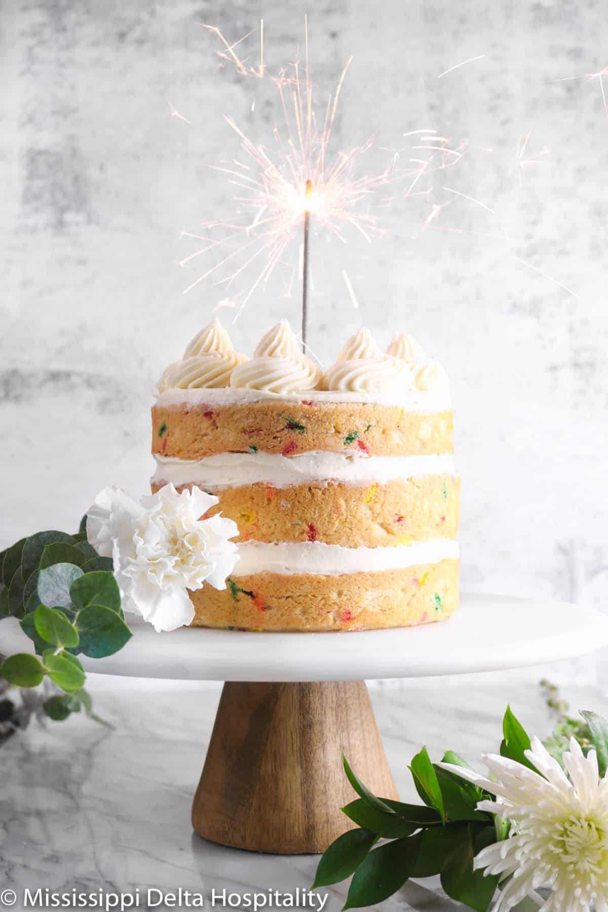 funfetti cake with a sparkler and white flowers on a marble cake plate