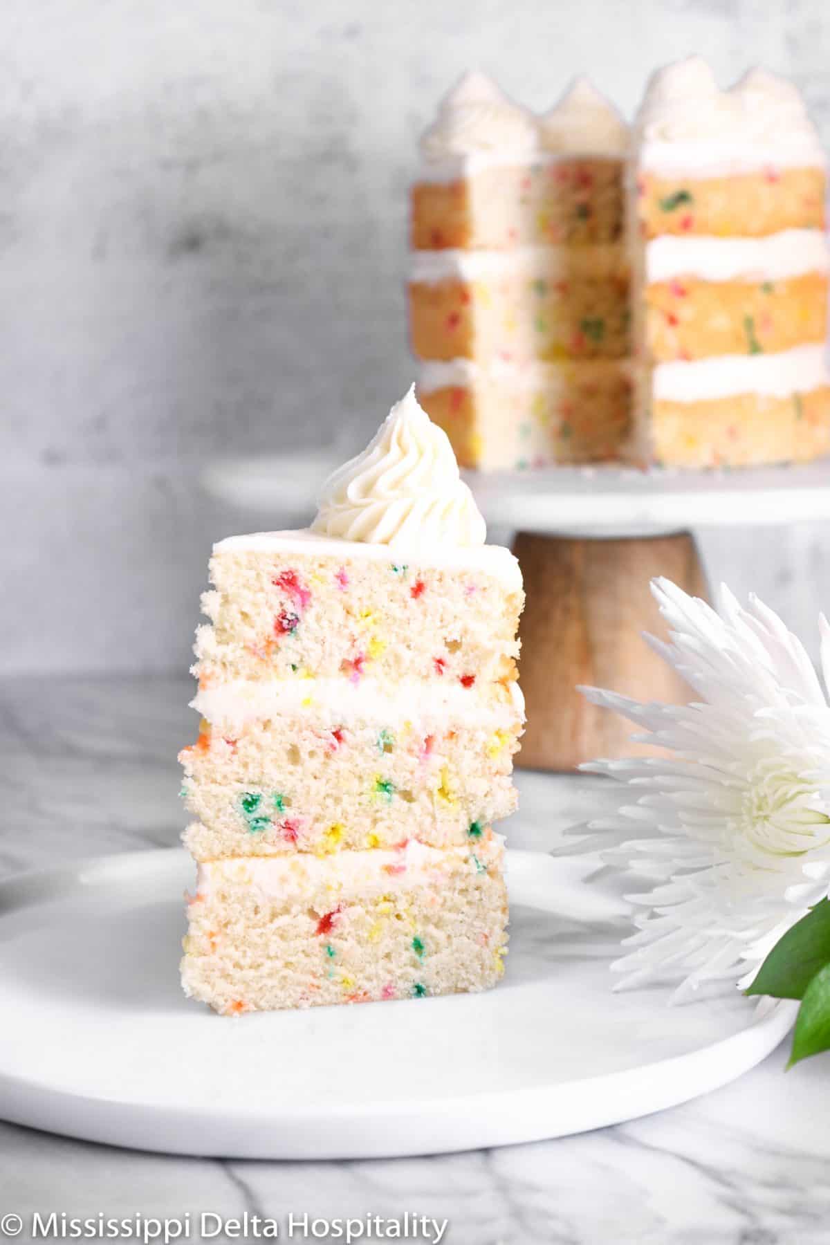 a slice of funfetti cake on a white plate with a flower