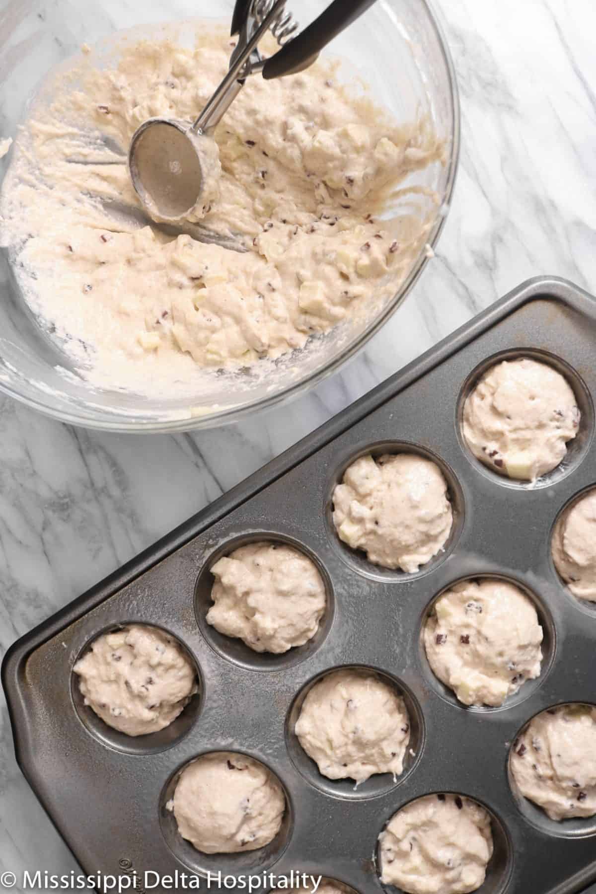 a muffin tin filled with batter and a glass bowl on a marble board