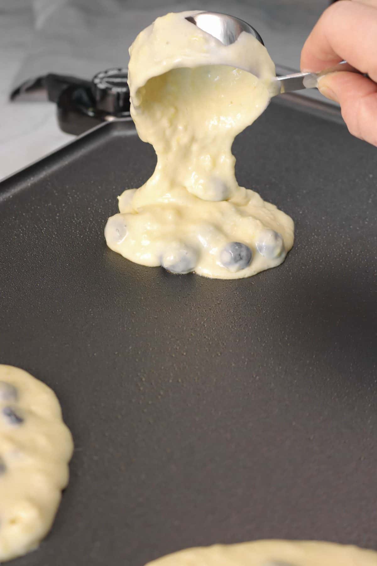 blueberry pancake batter being poured onto a griddle