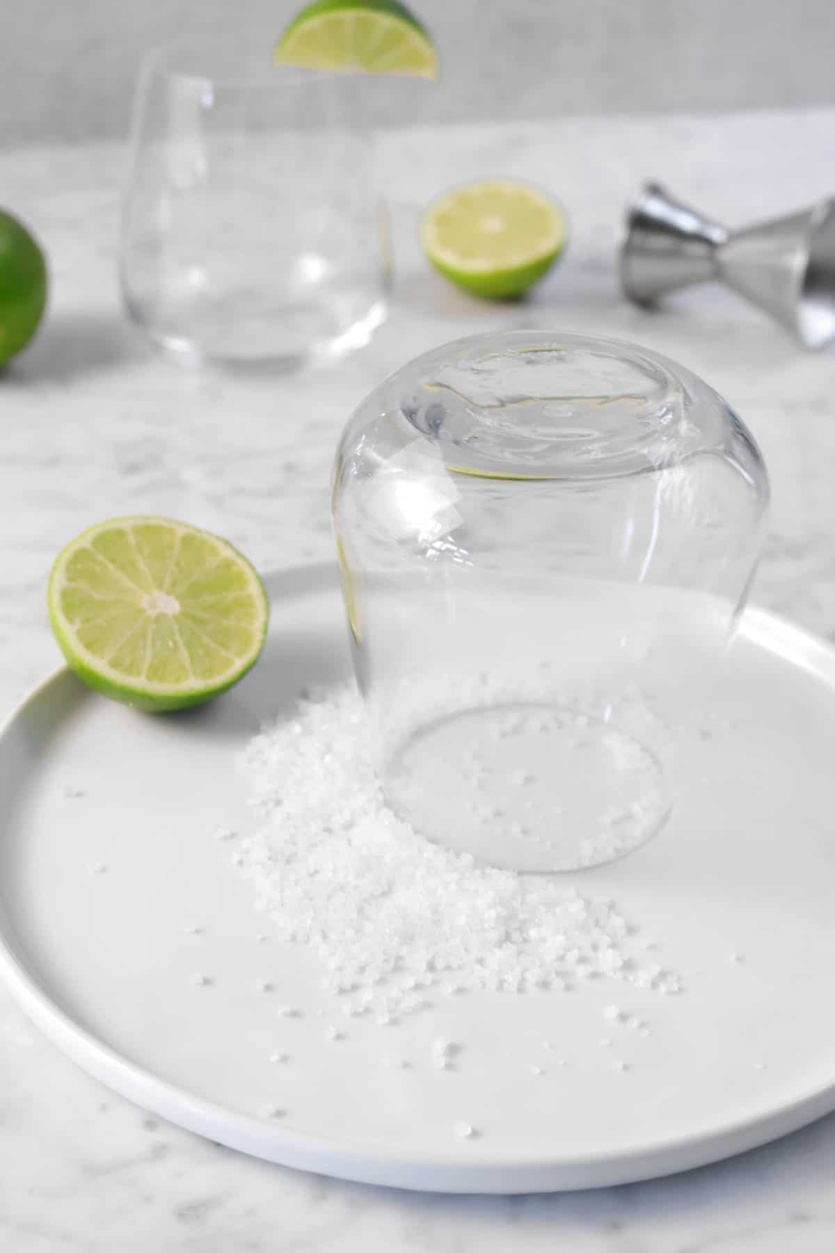 a glass turned upside down pressed against salt with lime slices on a marble board