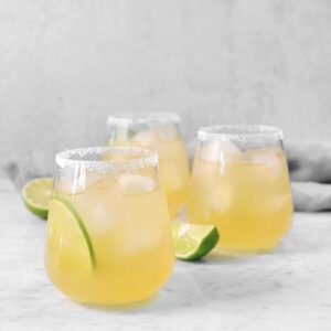 three lime margaritas on a marble board with slices of lime and a grey napkin