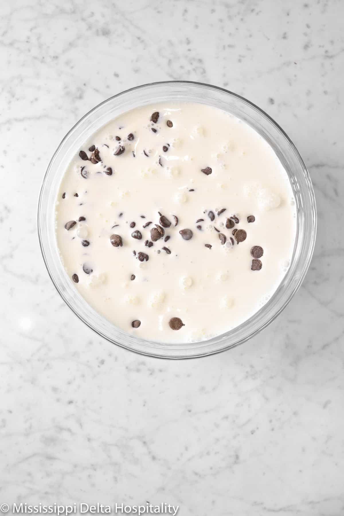chocolate chips and milk in a glass bowl on a marble board
