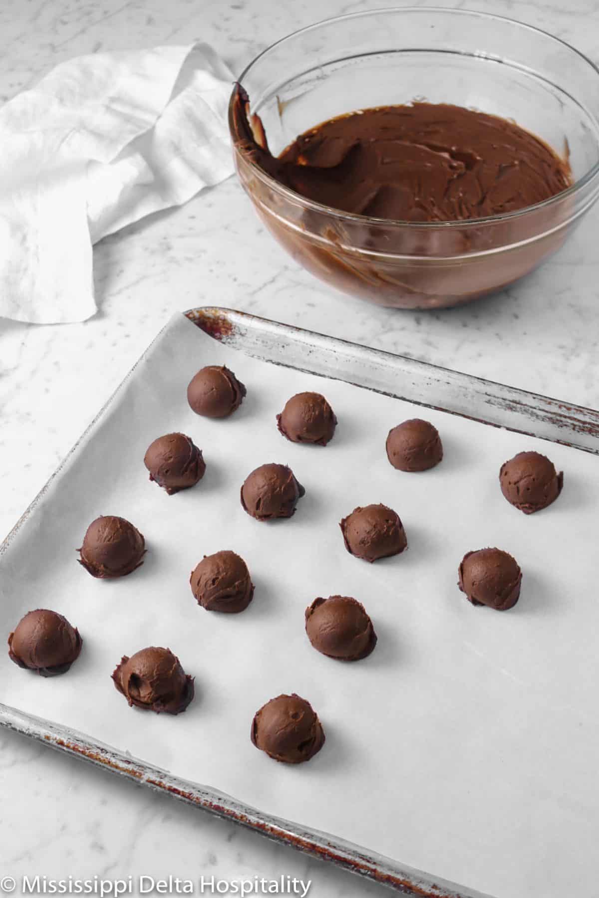 small balls of ganache on a baking sheet with a glass bowl of ganache and a white napkin