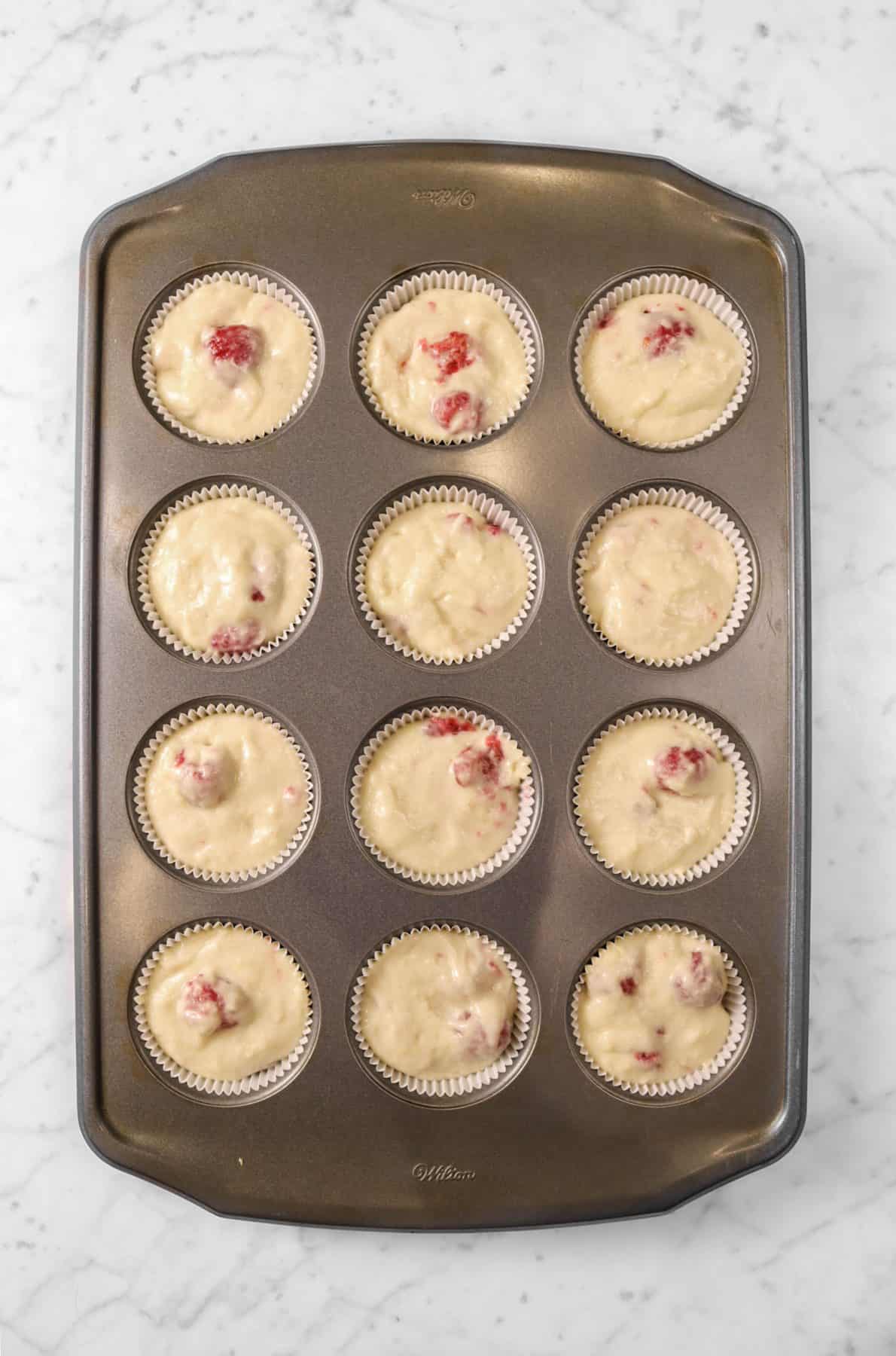raspberry muffin batter in a muffin pan on a marble board