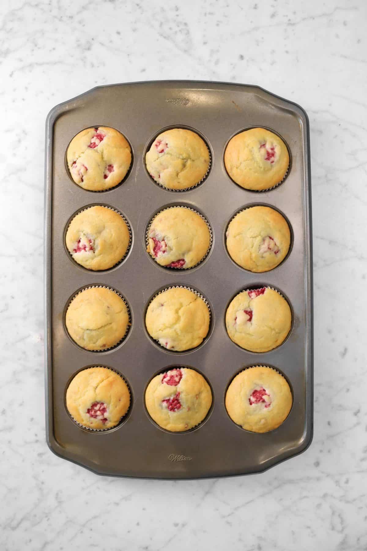 raspberry muffins in a muffin pan on a marble board