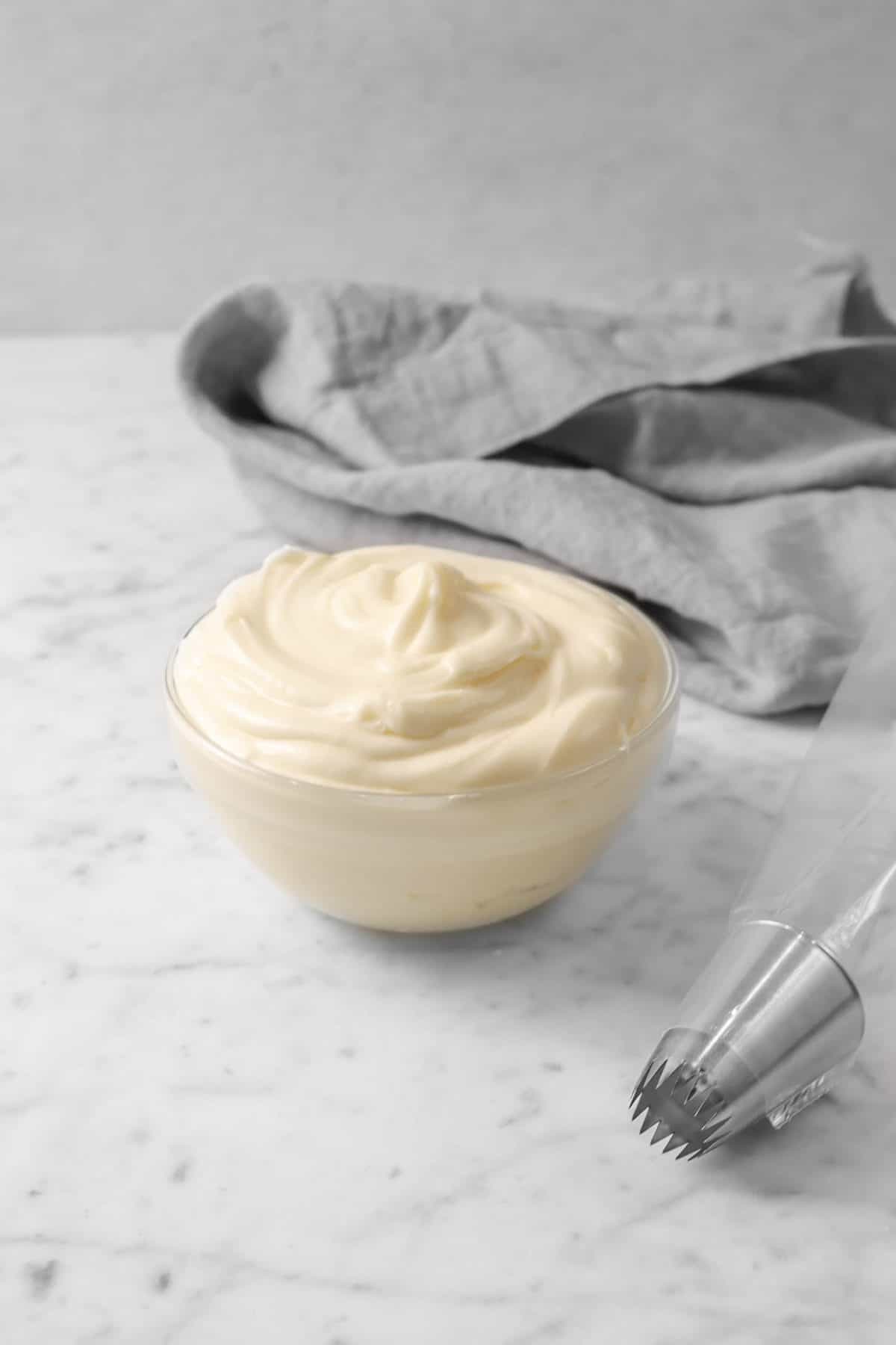 small bowl of cream cheese frosting in a glass bowl with a piping bag and a grey napkin
