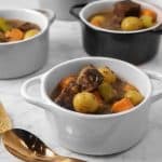 four bowls of beef stew with a copper spoon and thyme sprigs