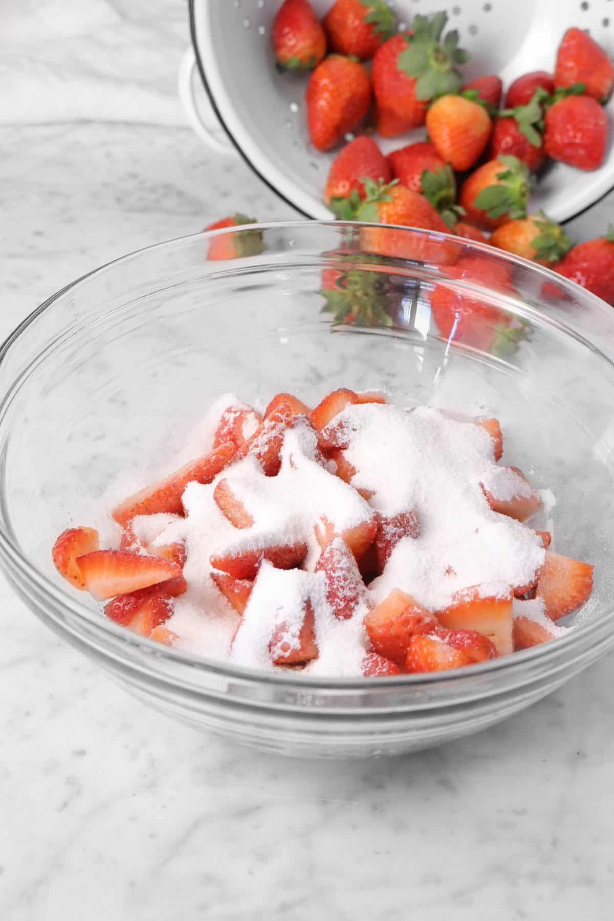 sugar on top of the strawberries in a glass bowl