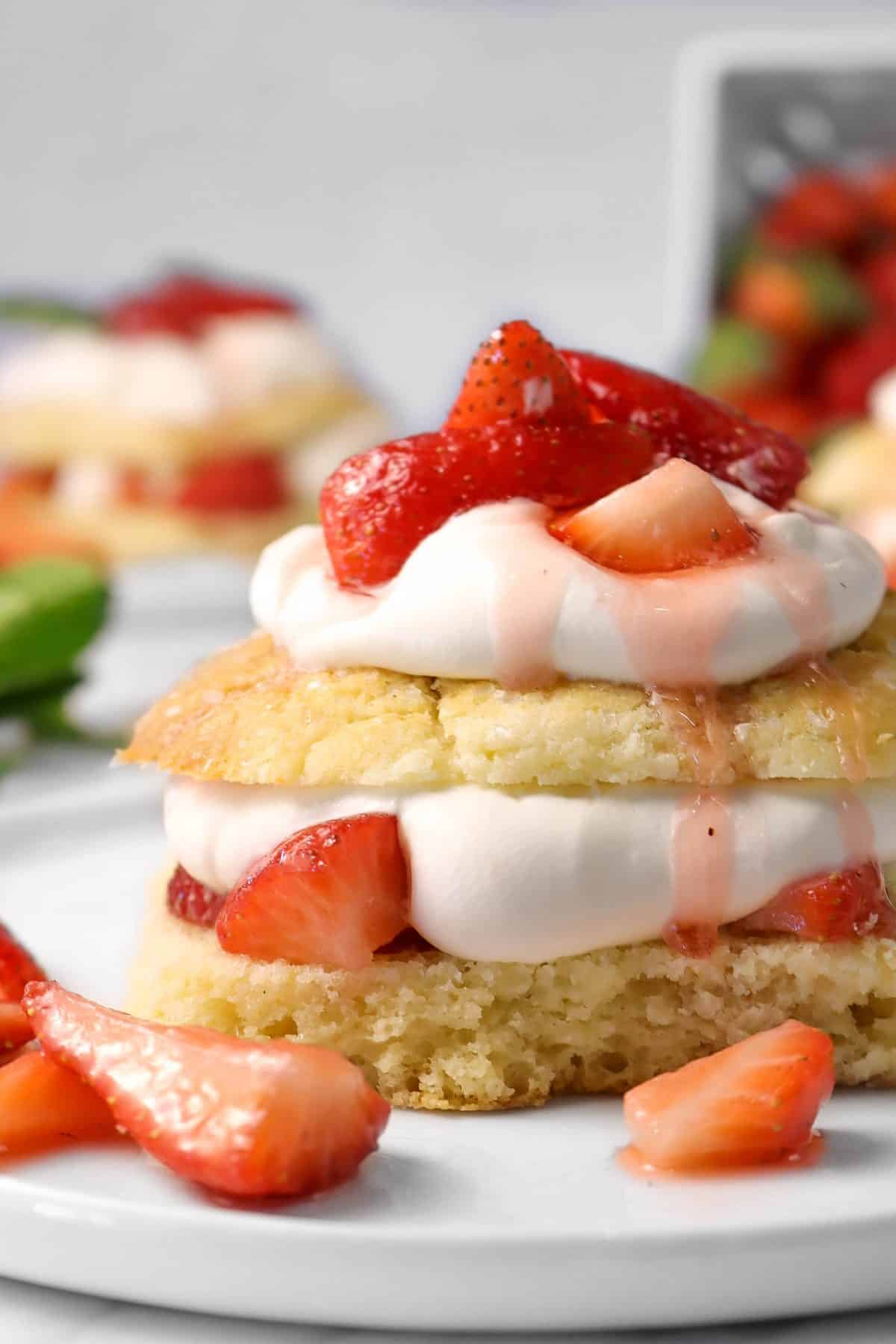 strawberry shortcake on a white plate with chopped strawberries on the plate with another shortcake in the background
