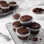 chocolate muffins on a cooling rack with chocolate chips and white lates and a napkin