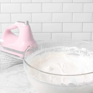 a bowl of chantilly cream on a marble counter with a pink hand mixer