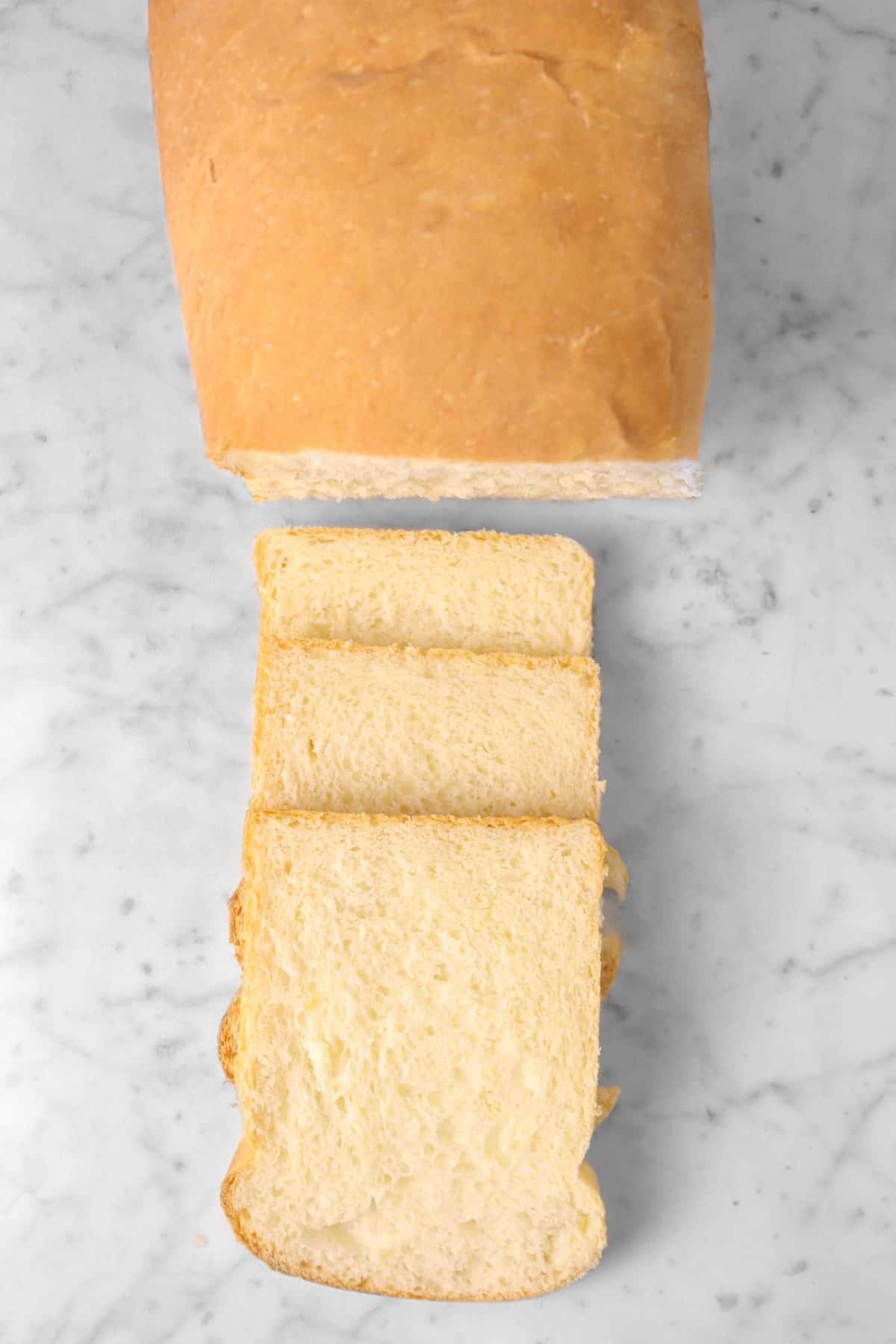 bread loaf on a marble counter with three slices laid out in front