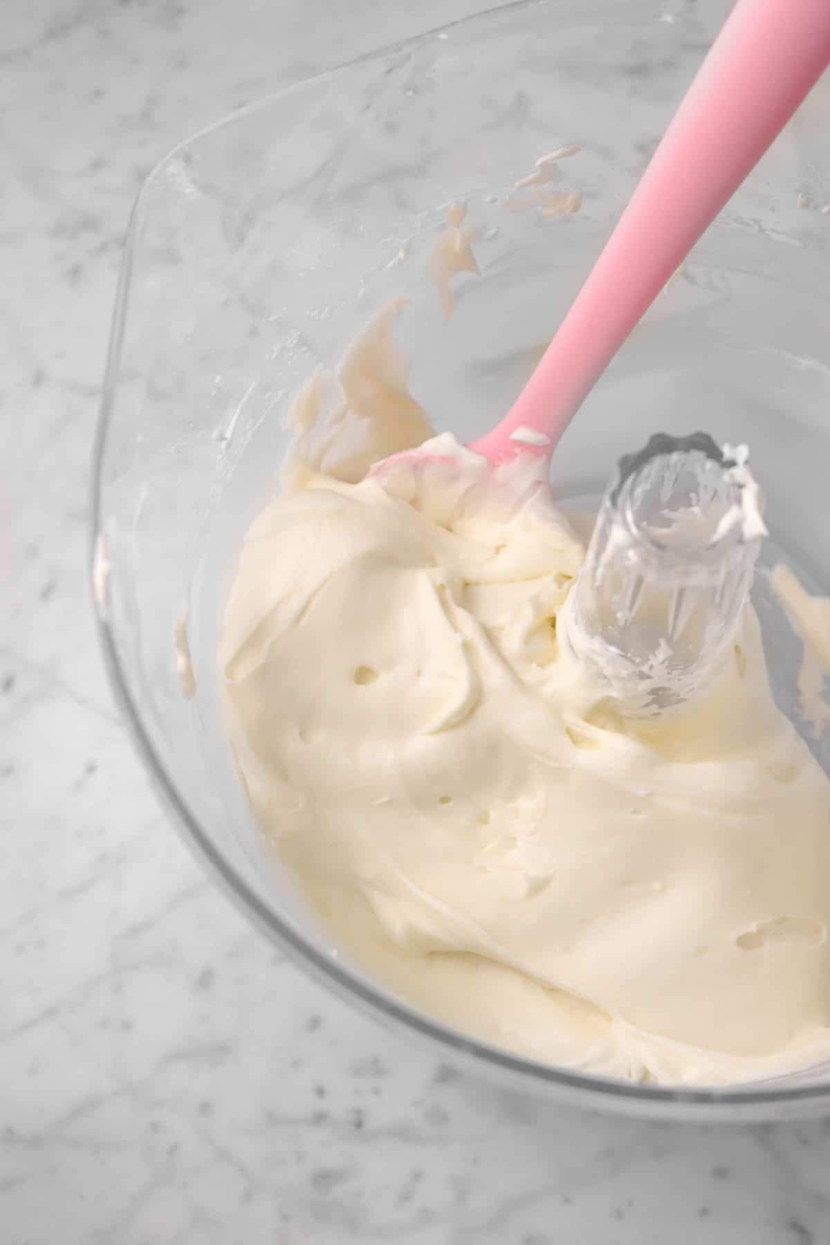 a bowl of cream cheese frosting with a pink spatula