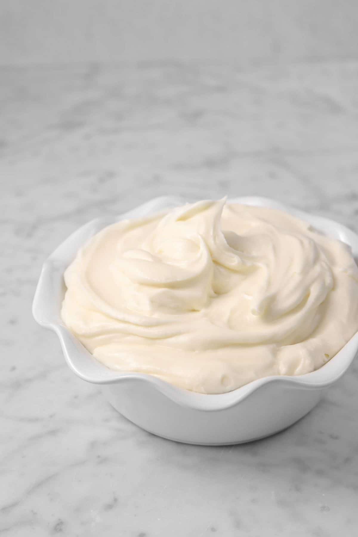 a white bowl of cream cheese frosting on a marble board