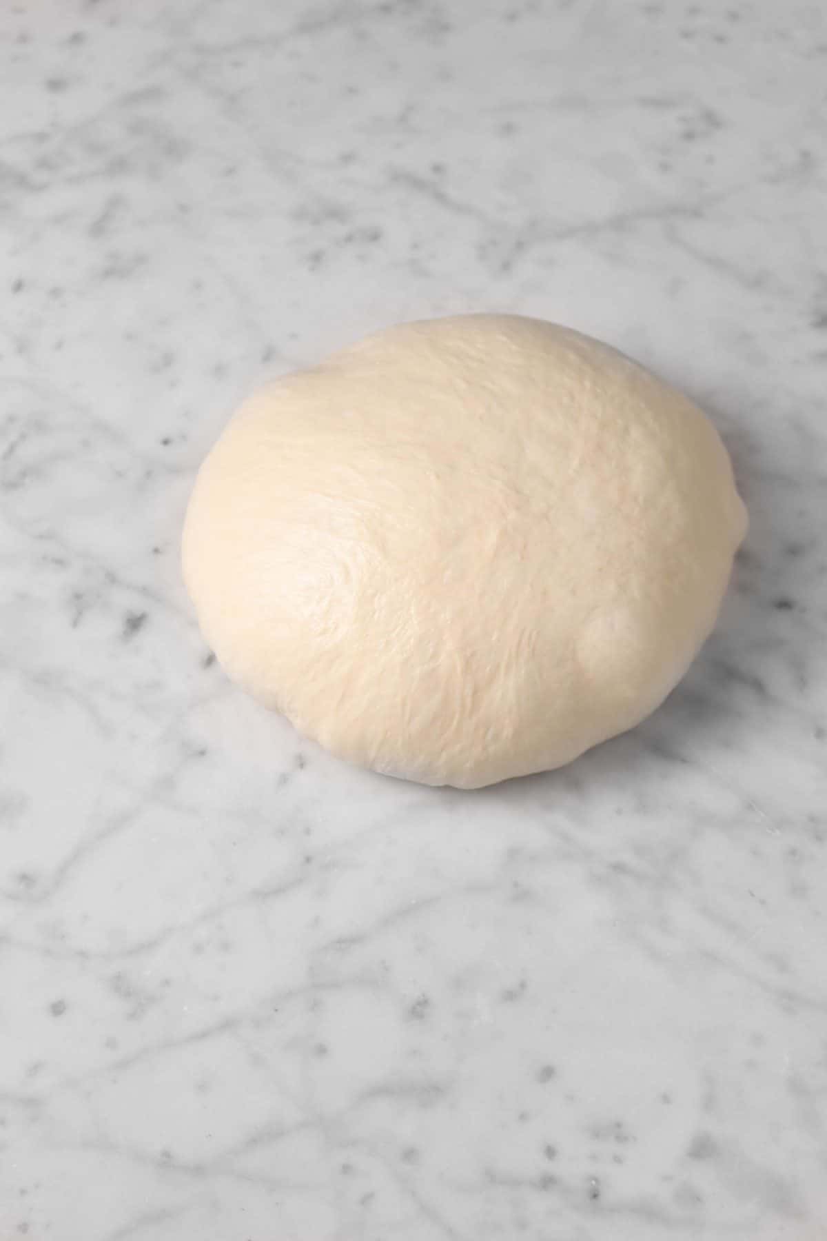 dough smoothened out in a small boule on a marble board
