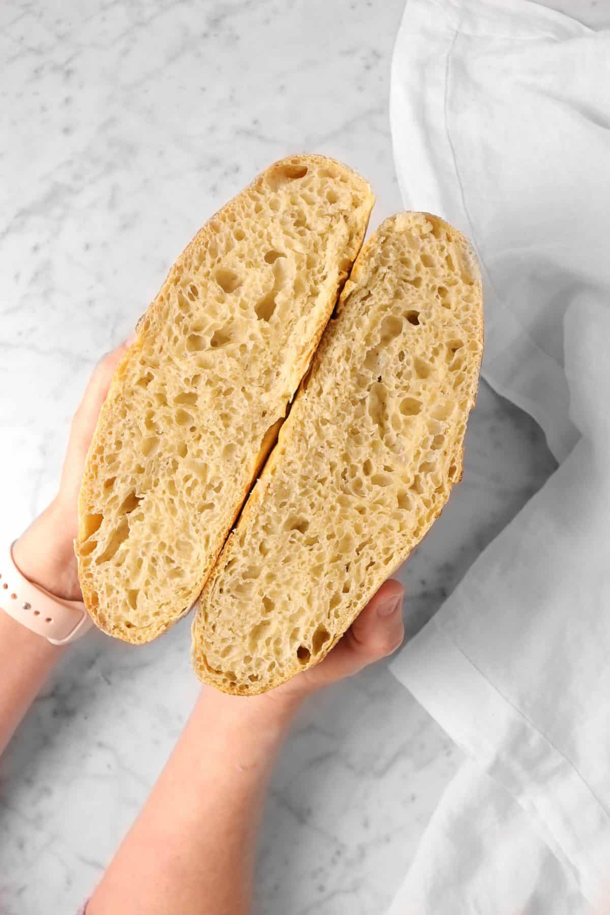 sourdough bread sliced in half being held up right on a marble counter with a white napkin