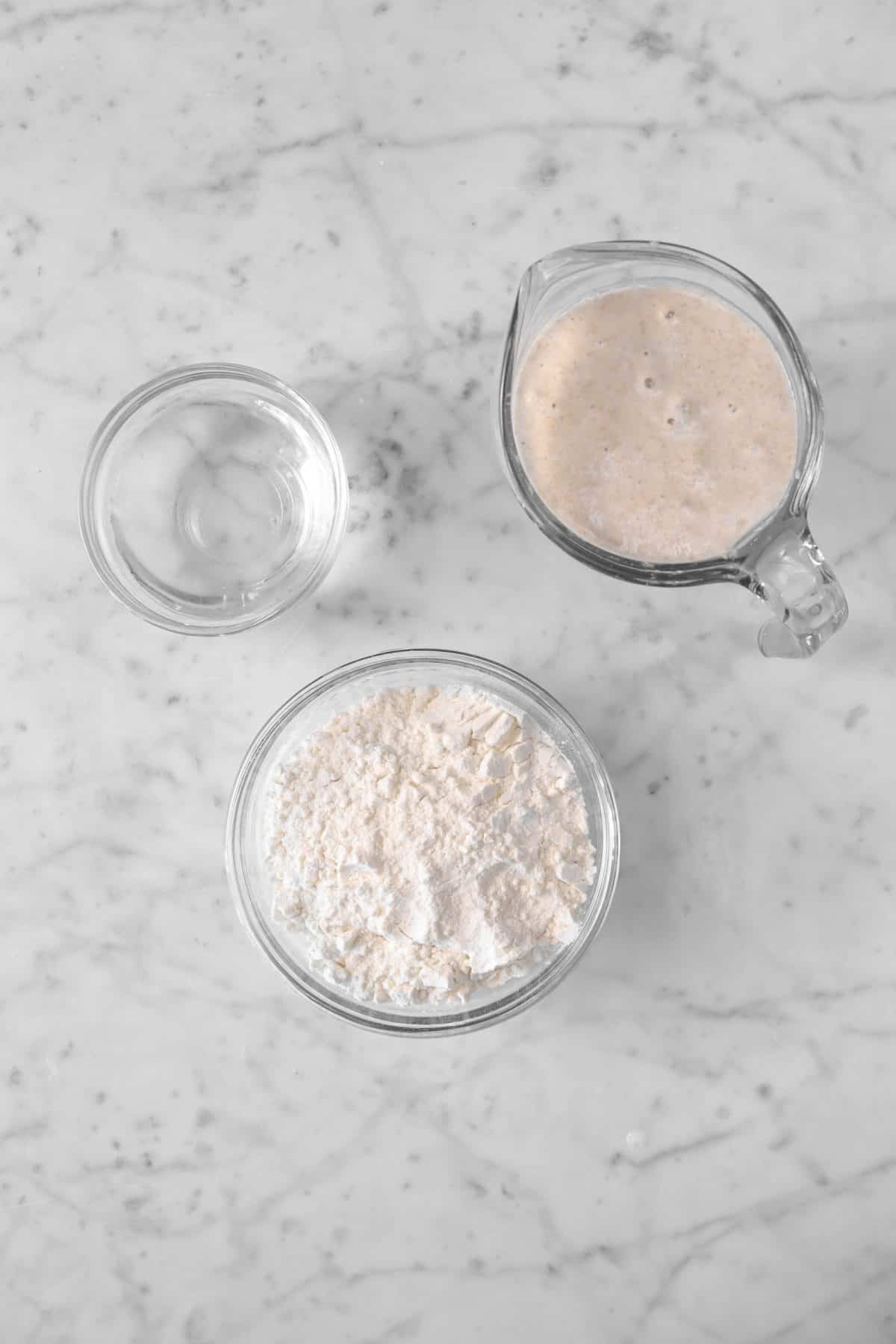 sourdough starter, flour, and water on a marble counter