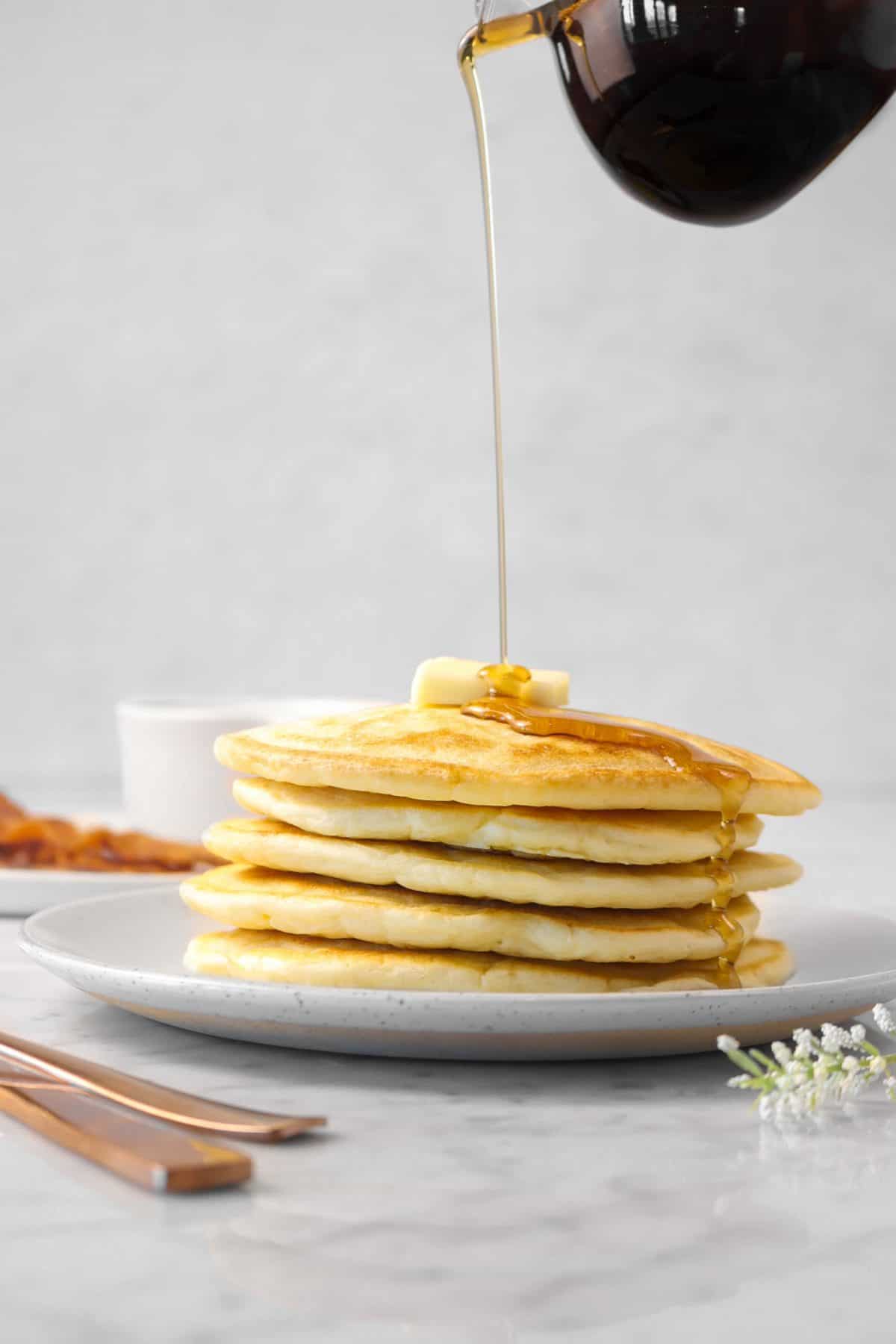 maple syrup being poured on a stack of five sourdough pancakes on a white plate 