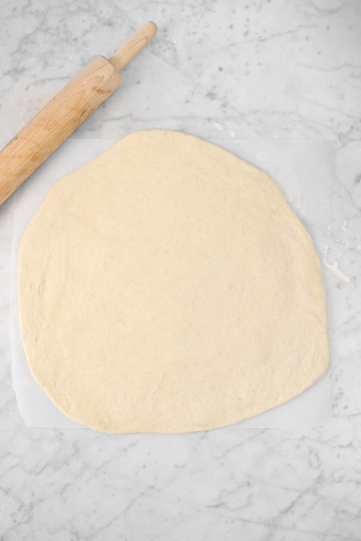 pizza dough rolled out into a circle on a piece of parchment with a wood rolling pin