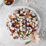 a pie plate with popcorn mix on a marble counter with fresh flowers, a bowl of M&m's, and a white napkin
