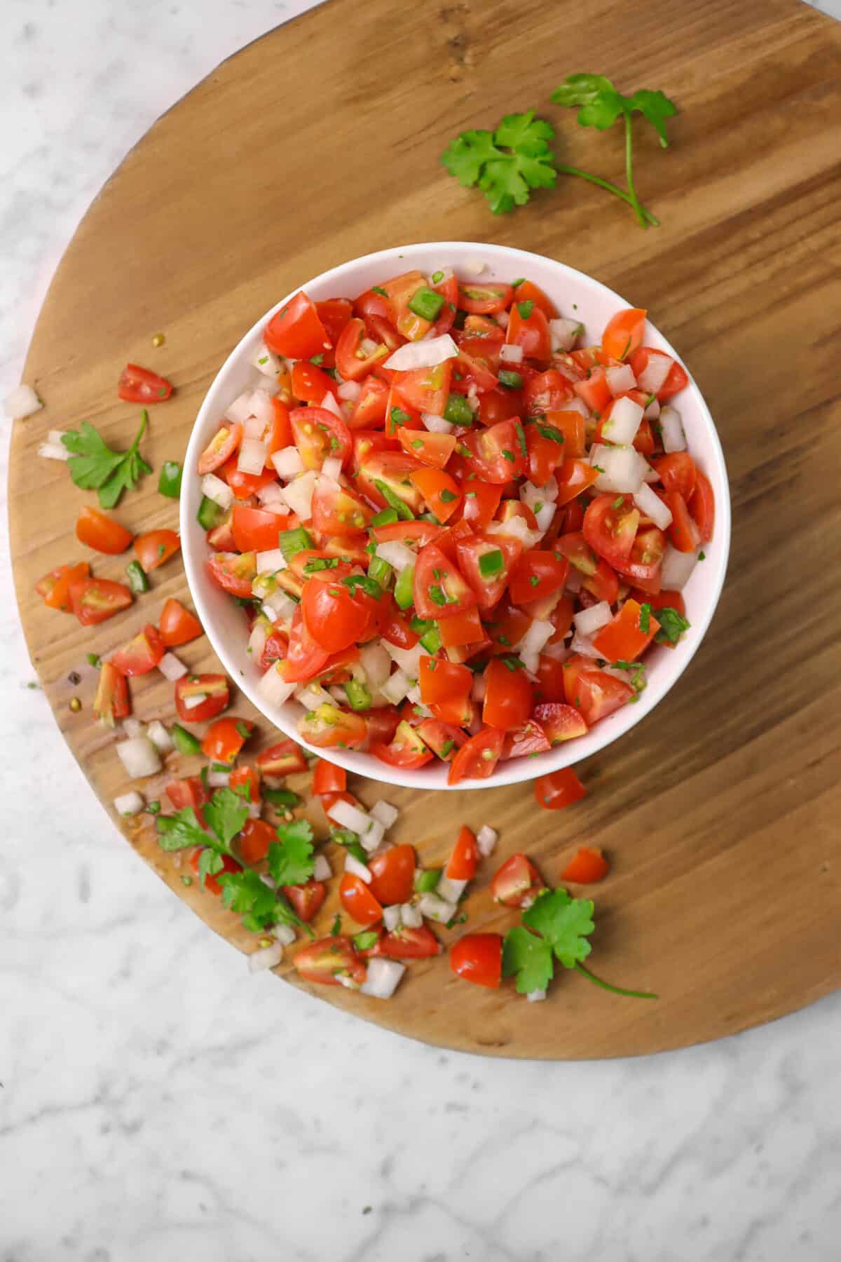 tomato salsa on a circle wood board with spilled salsa with cilantro leaves