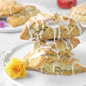 three lemon poppyseed scones with fresh flowers, more scones in the back, and a jar of jam