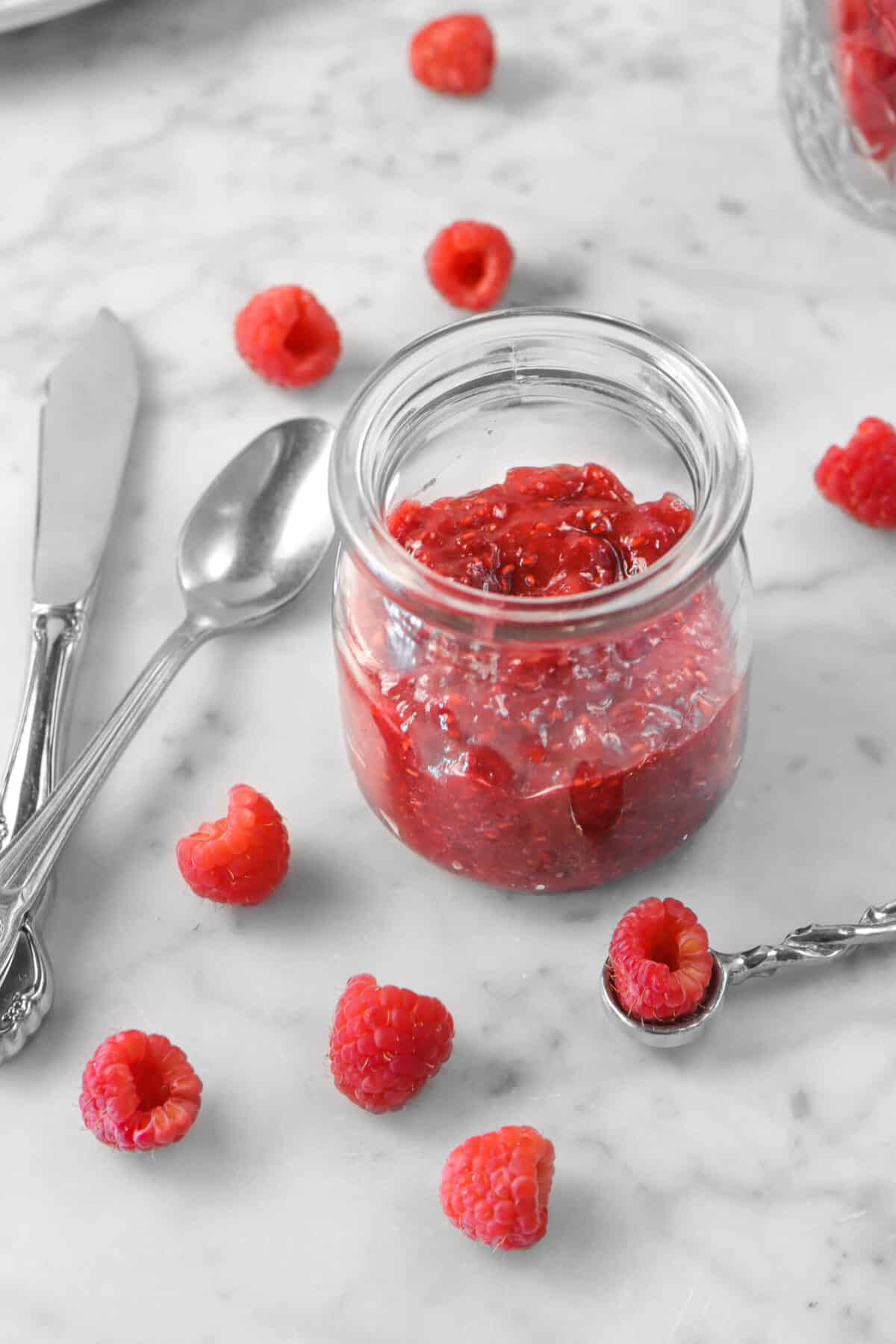 raspberry jam in a glass jar with fresh raspberries and silverware 