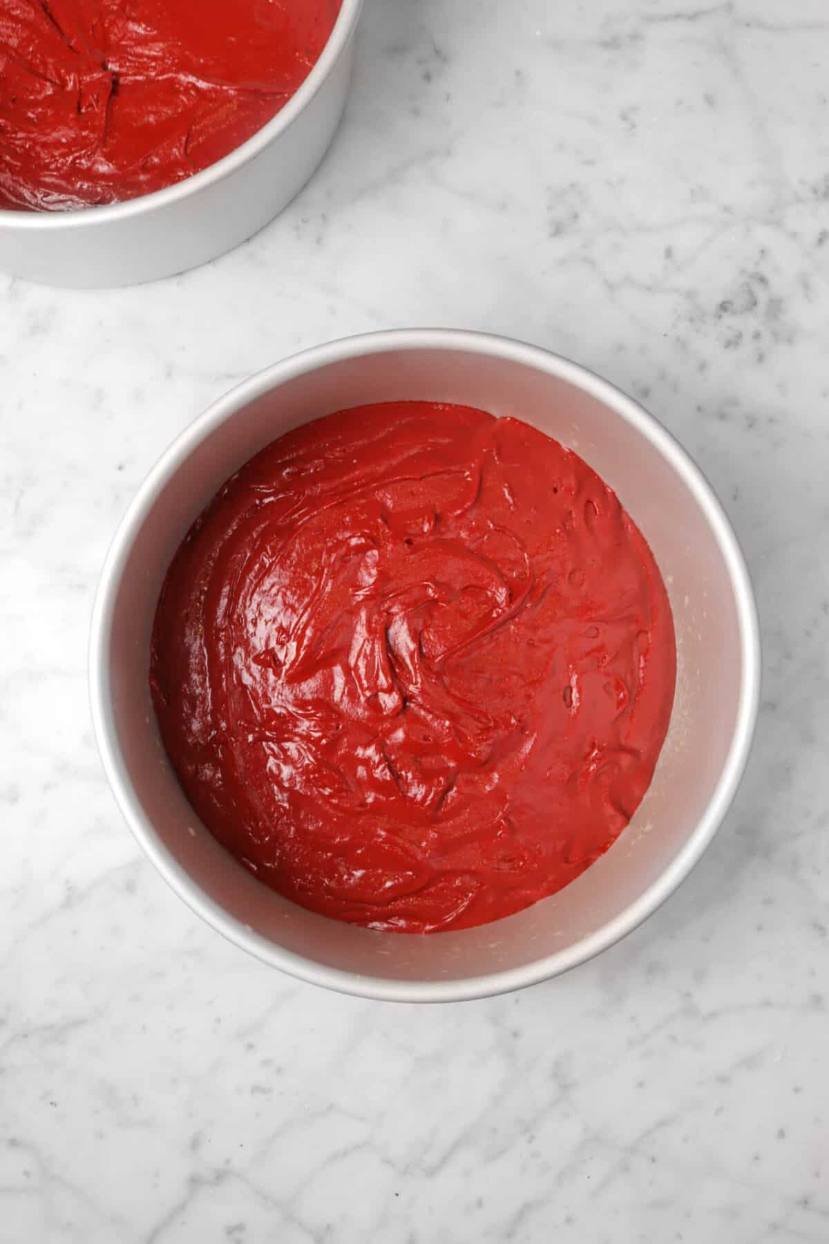 red velvet cake batter in a round cake pan on a marble counter
