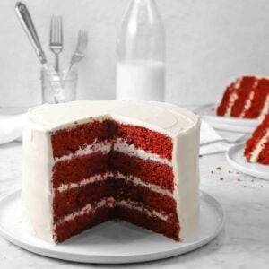 red velvet cake on a white plate with a jug of milk, a jar of forks, and two slices of cake
