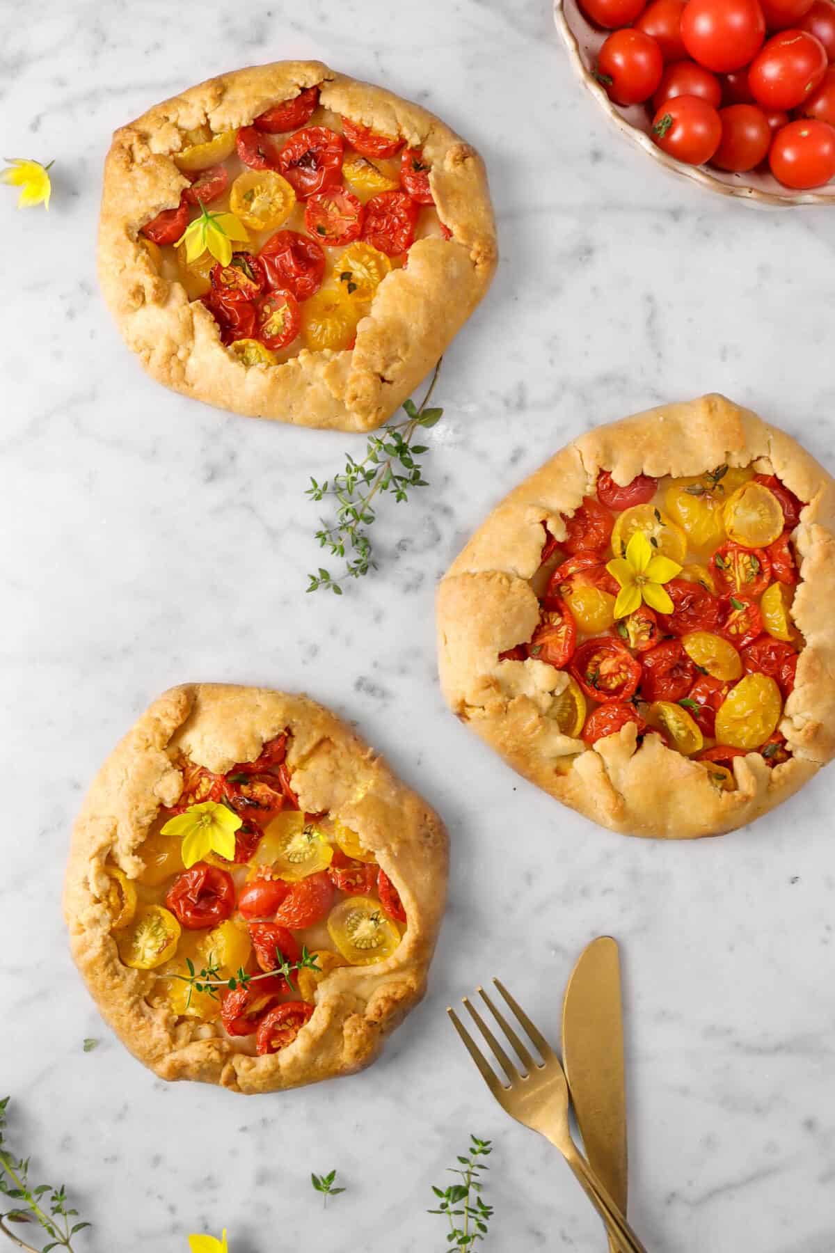 three galettes with tomato bowl, gold fork and knife, thyme sprigs, and flowers