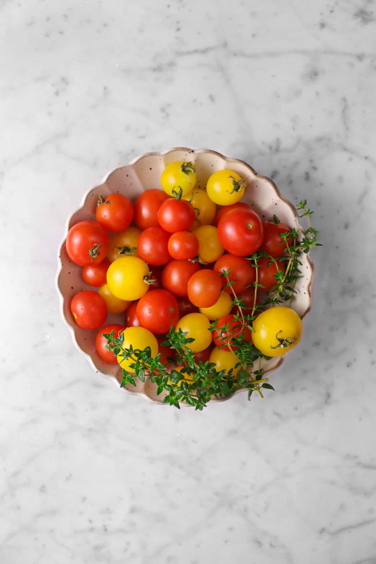 yellow and red tomatoes and thyme in small scalloped bowl