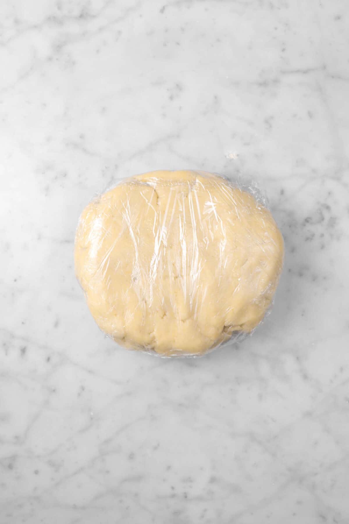 pie dough wrapped in plastic wrap on a marble surface