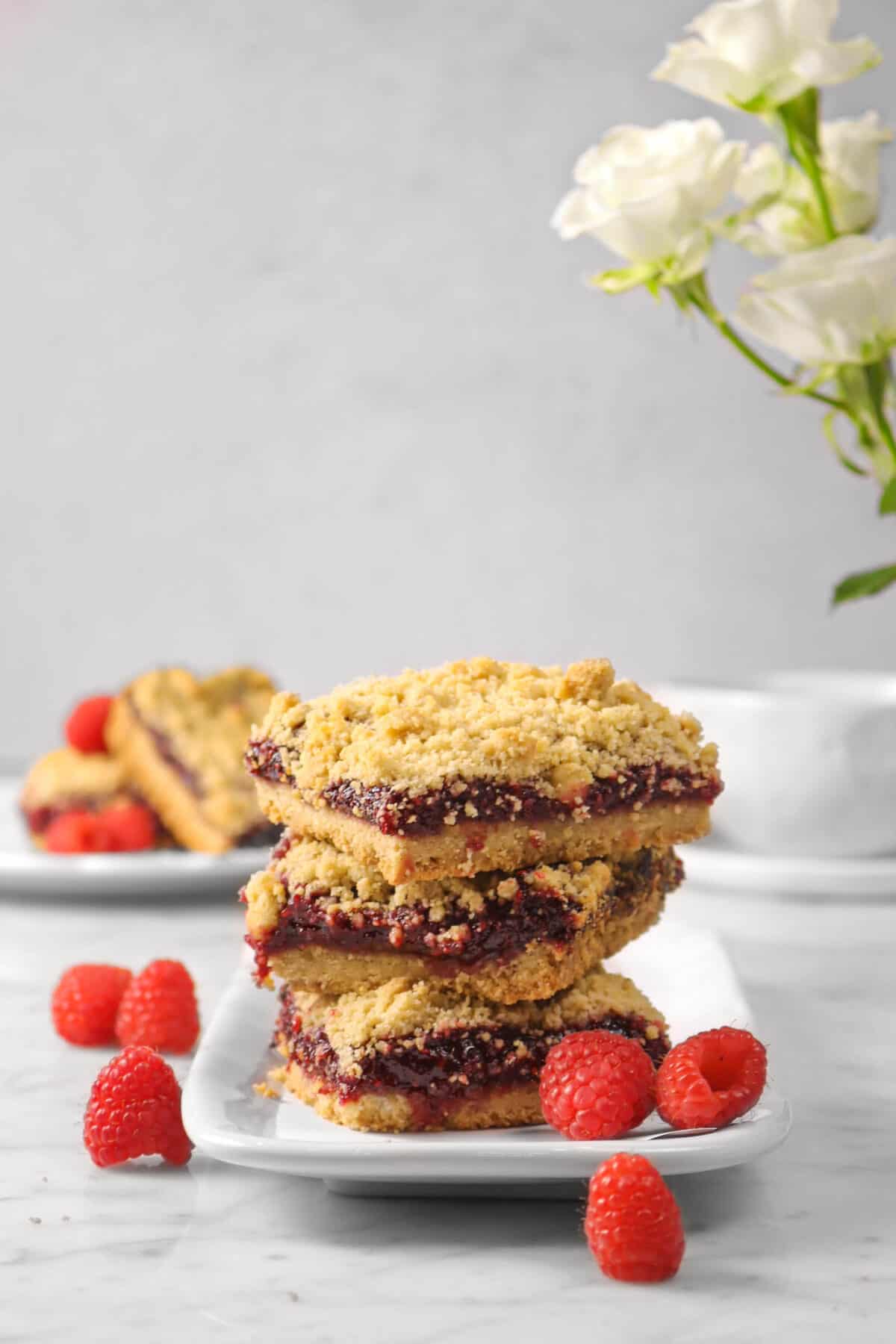three crumble bars on a white plate with fresh raspberries and roses