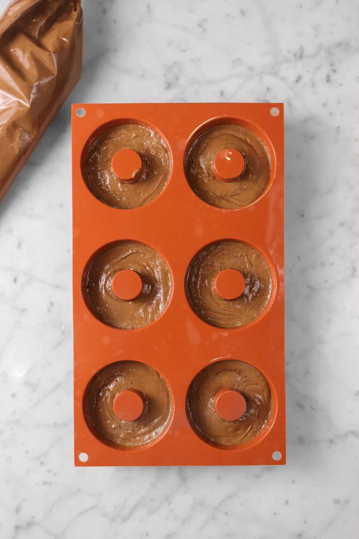 chocolate donut batter piped into donut molds on a marble counter